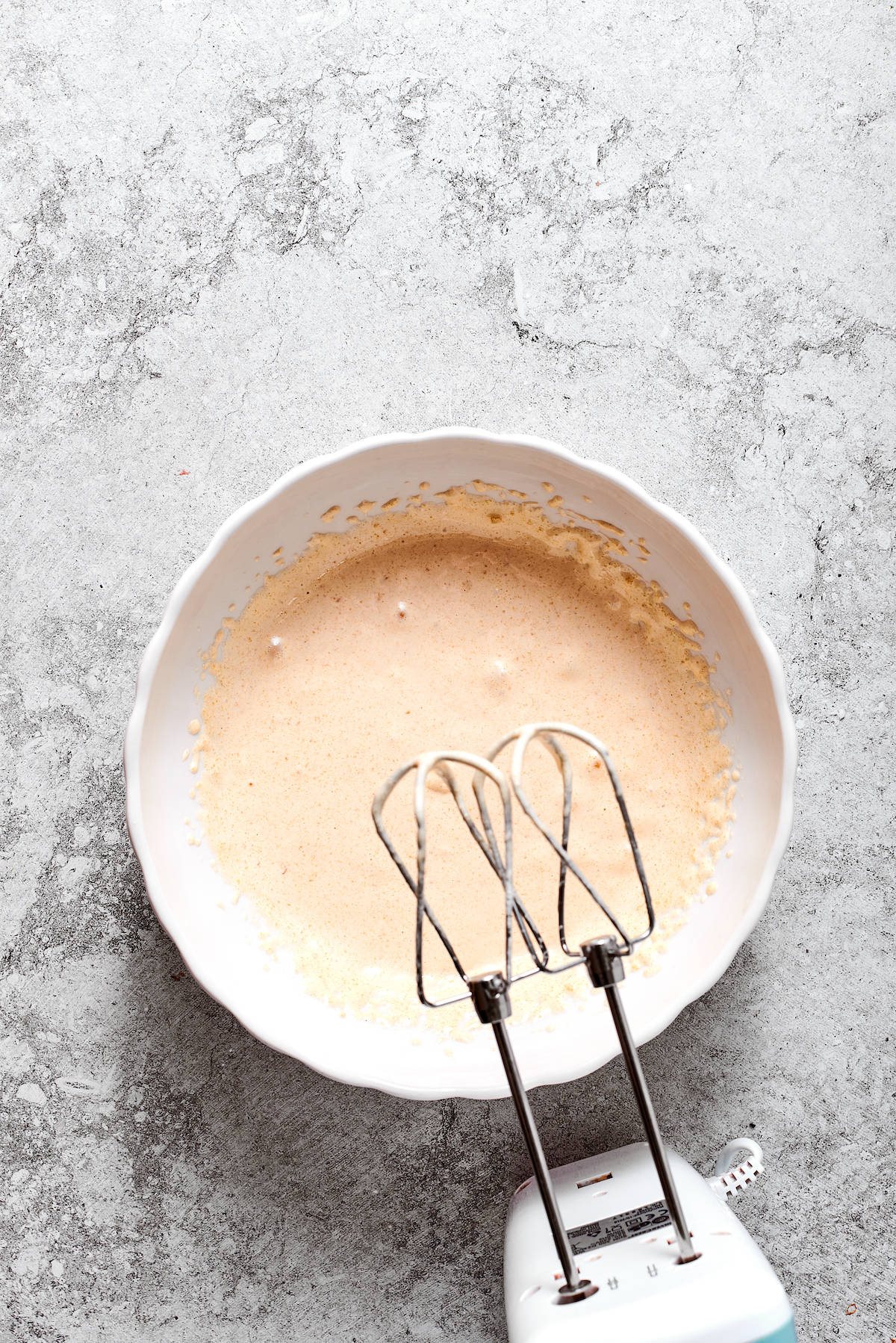 A hand mixer about to mix the warmed egg mixture in a bowl.