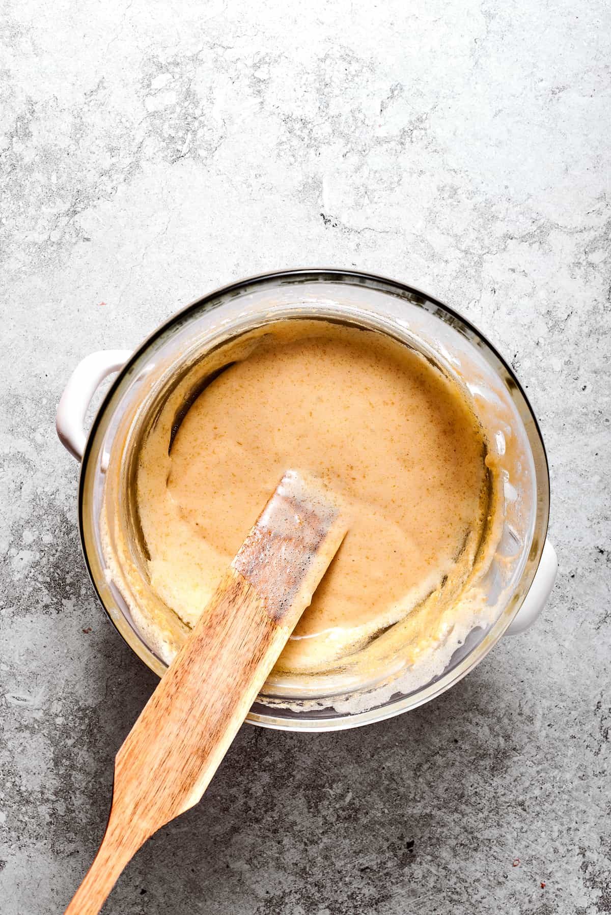 A spatula stirs a bowl of eggs and sugar set over simmering water.