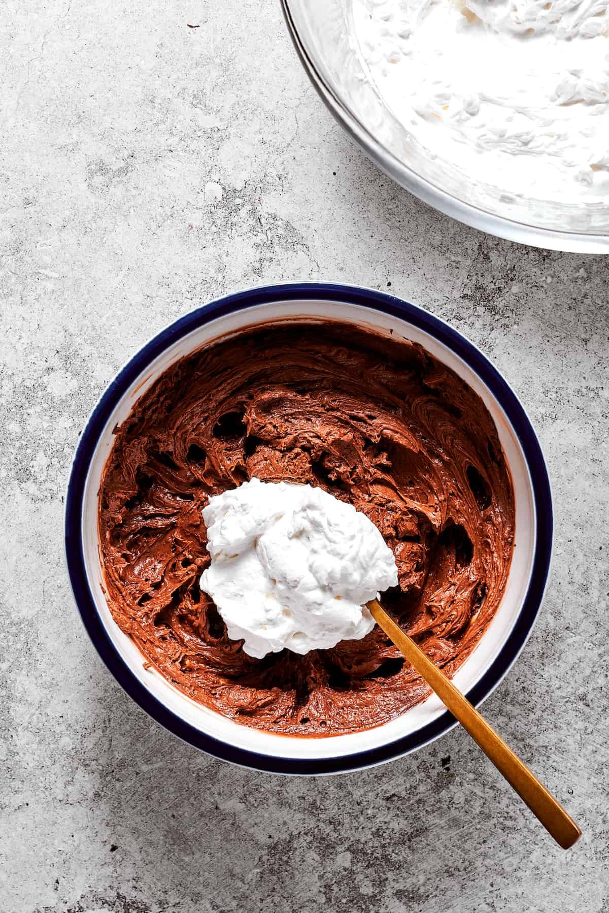A spoonful of whipped cream is folded into chocolate filling in a bowl.