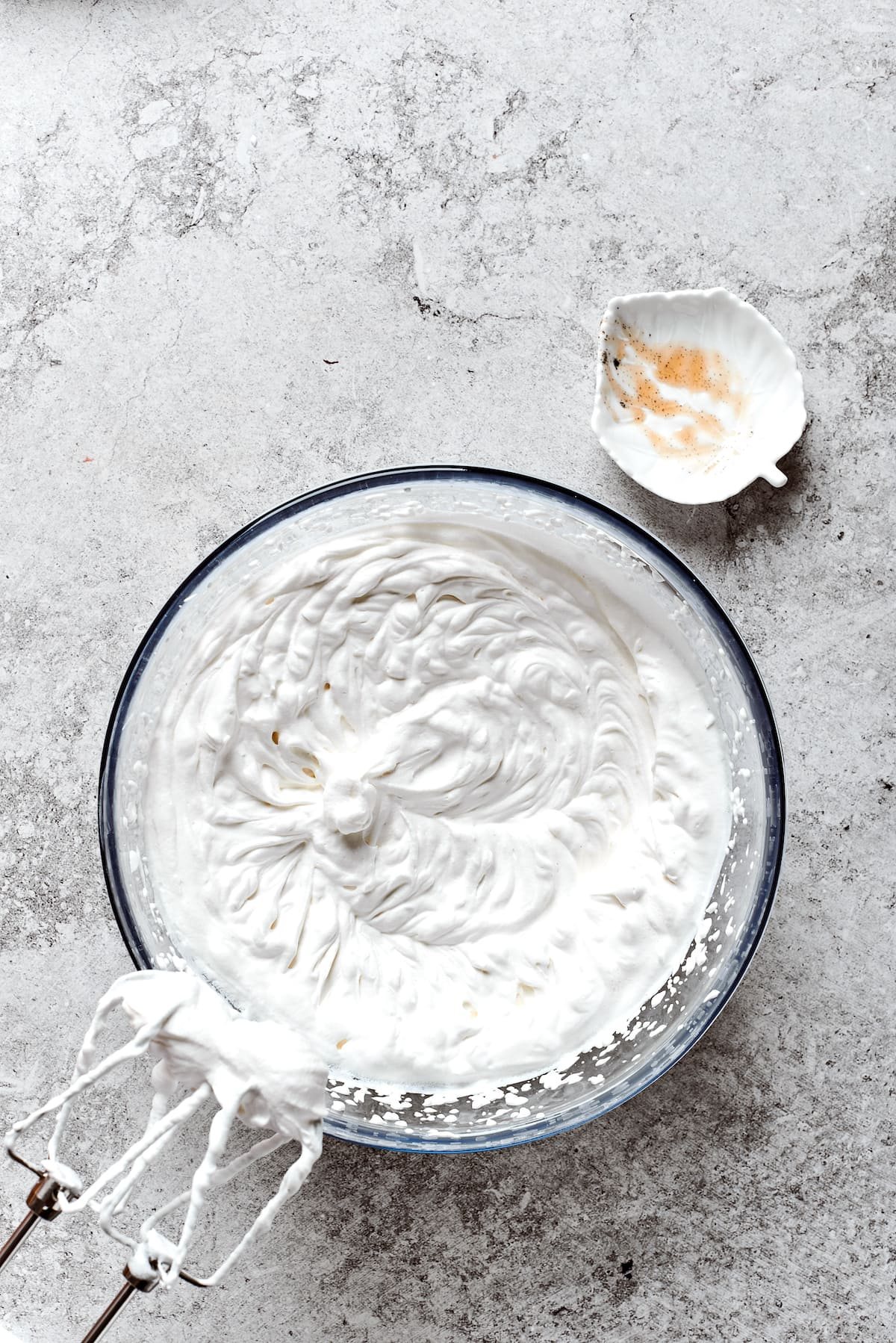 A bowl of freshly whipped cream with beaters above it.