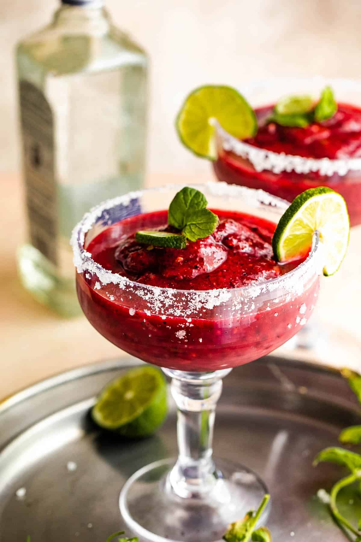 Frozen Berry Margarita served in a margarita glass with salted rims, slice of lime, and mint