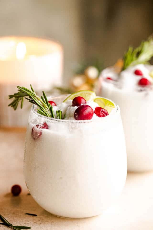 drinking glasses filled with white frozen margaritas and garnished with lime slices, rosemary sprigs, and cranberries