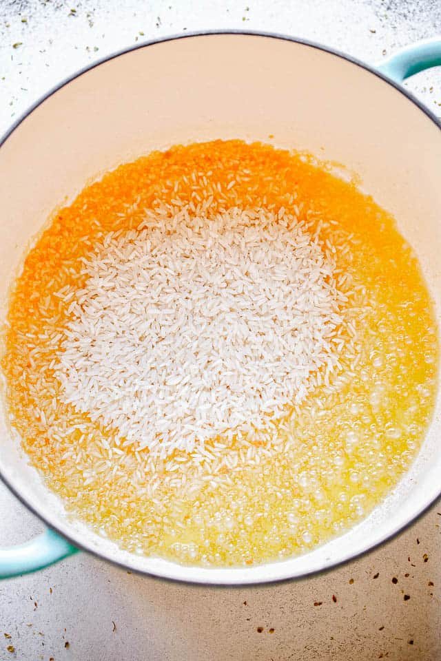 dutch oven with raw rice frying in butter