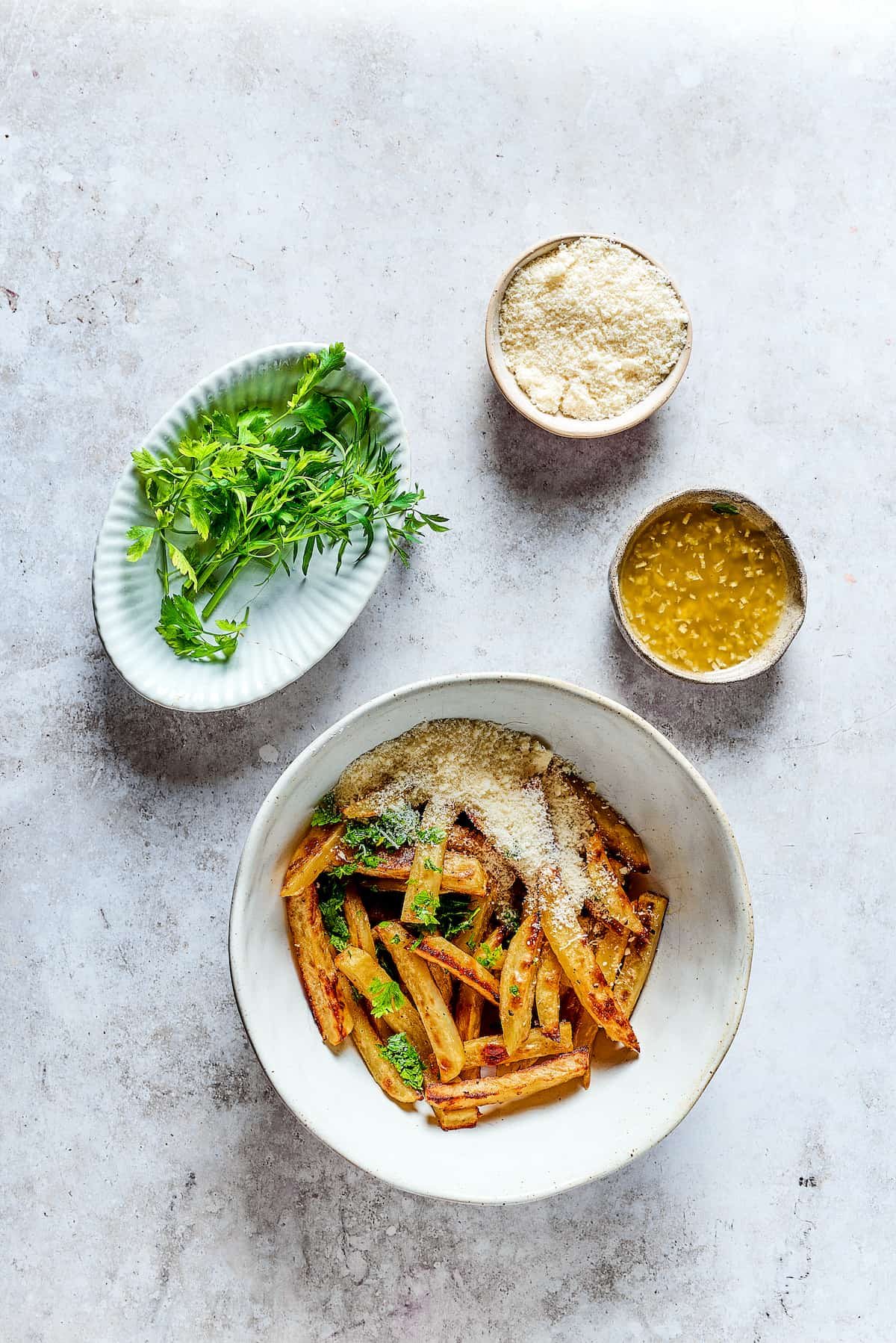 Baked fries in a bowl next to bowls of melted butter with garlic, parmesan, and parsley.