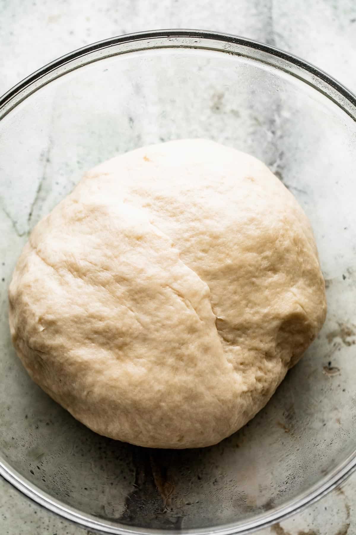a glass bowl with a ball of bread dough.