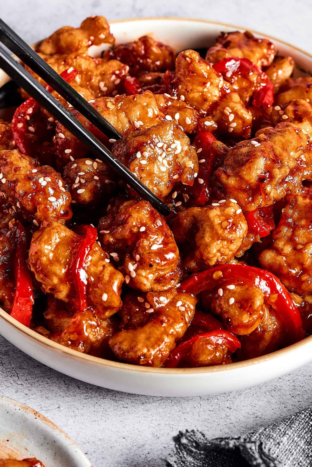 A pair of chopsticks picking up a piece of sticky chicken from a dish.