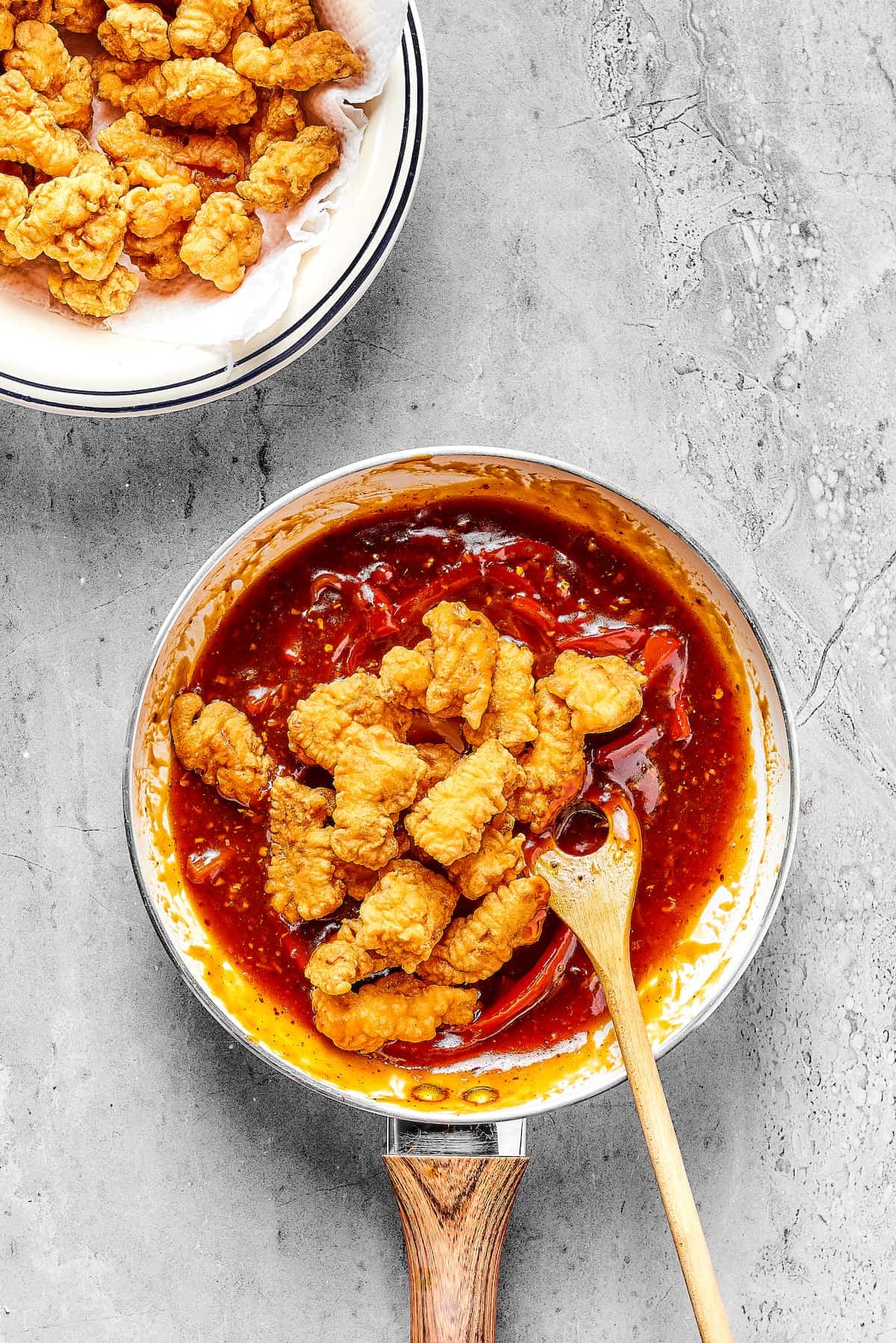 Fried chicken being tossed in a reddish sauce with bell peppers.