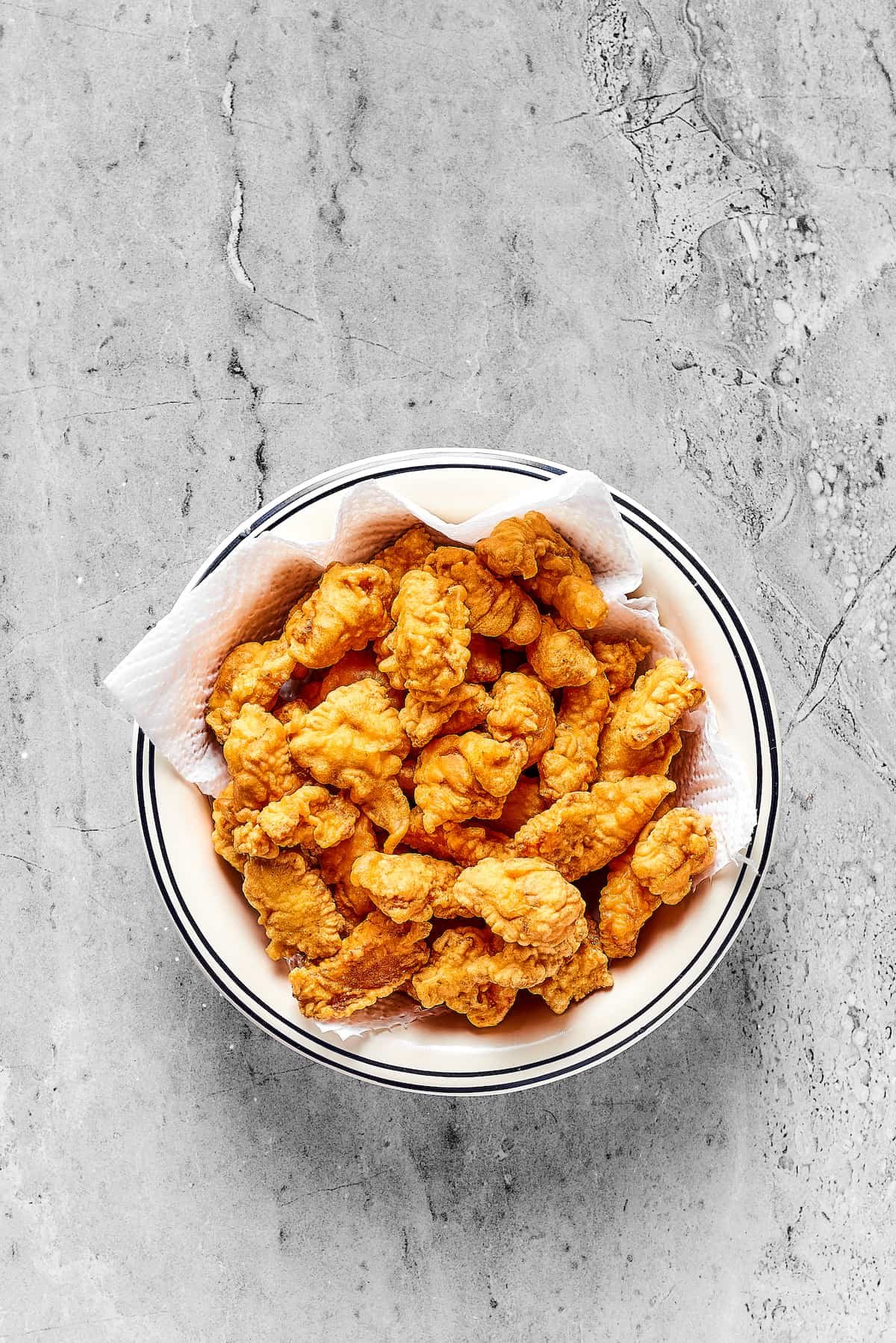 Fried chicken pieces draining on a paper-towel-lined platter.