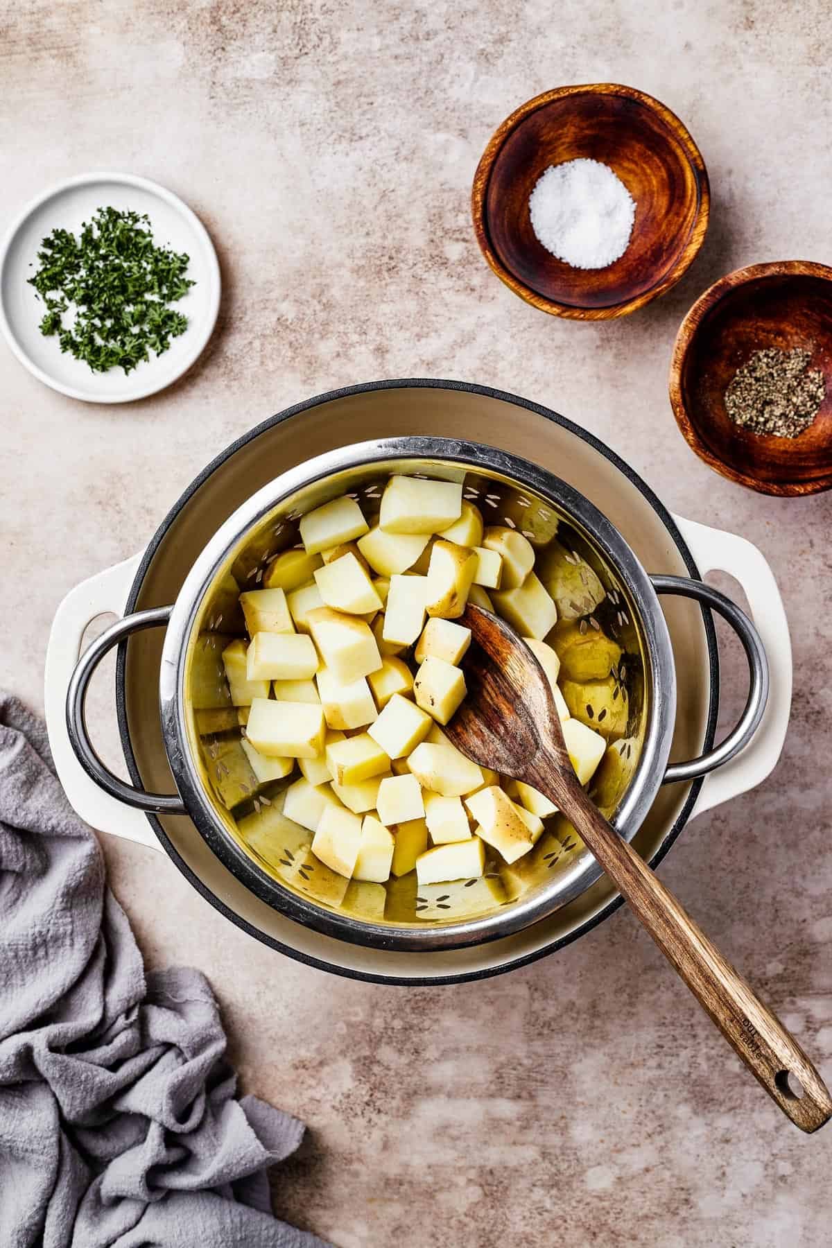 Potatoes boiling in a large pot. Dishes of parsley, salt, and pepper are arranged on the work surface.