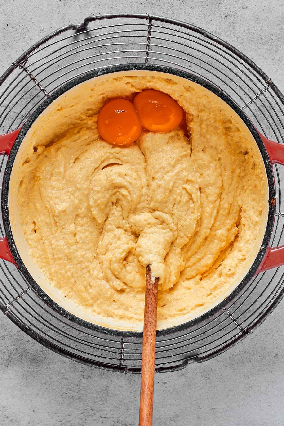 Creamy semolina batter with two egg yolks being stirred in.