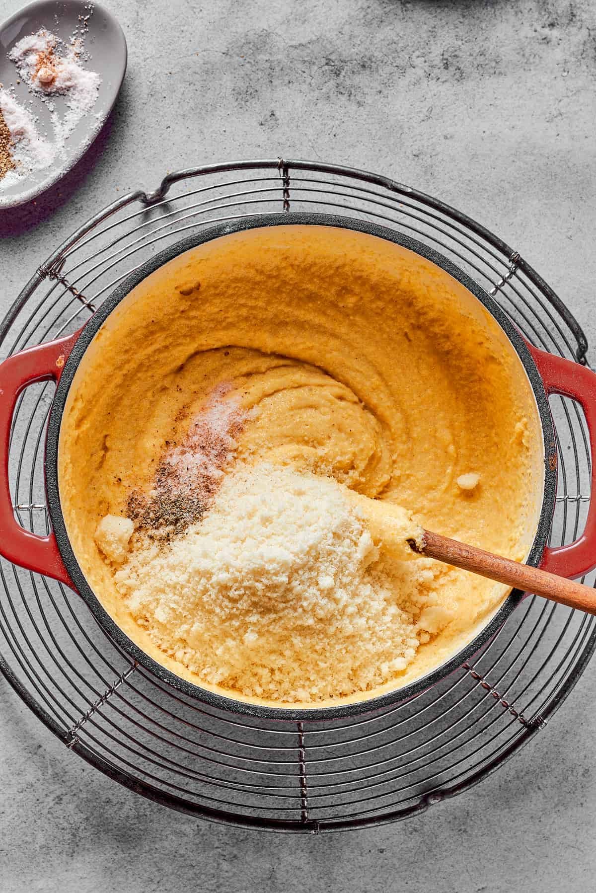 Overhead shot of parmesan cheese and seasonings being stirred into thick semolina batter.