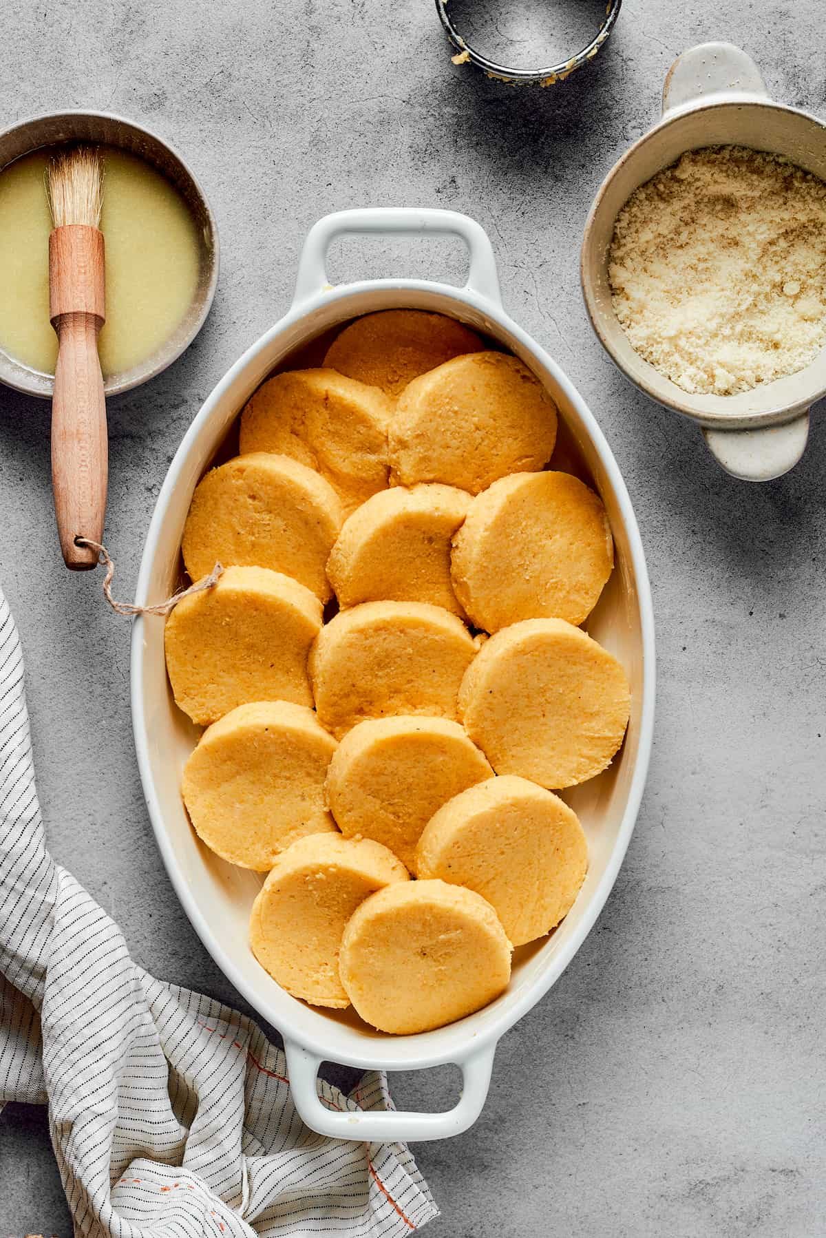 Circular semolina gnocchi layered into an oval baking dish.