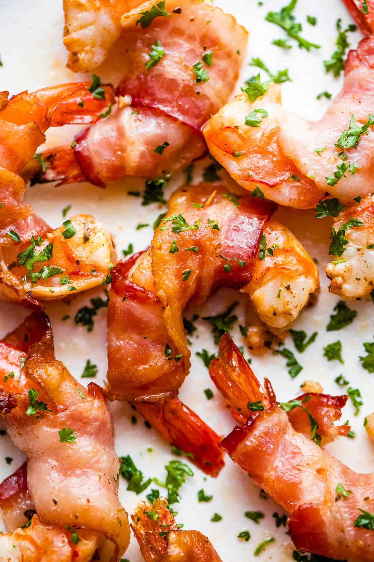 bacon wrapped shrimp arranged on a white plate and garnished with parsley