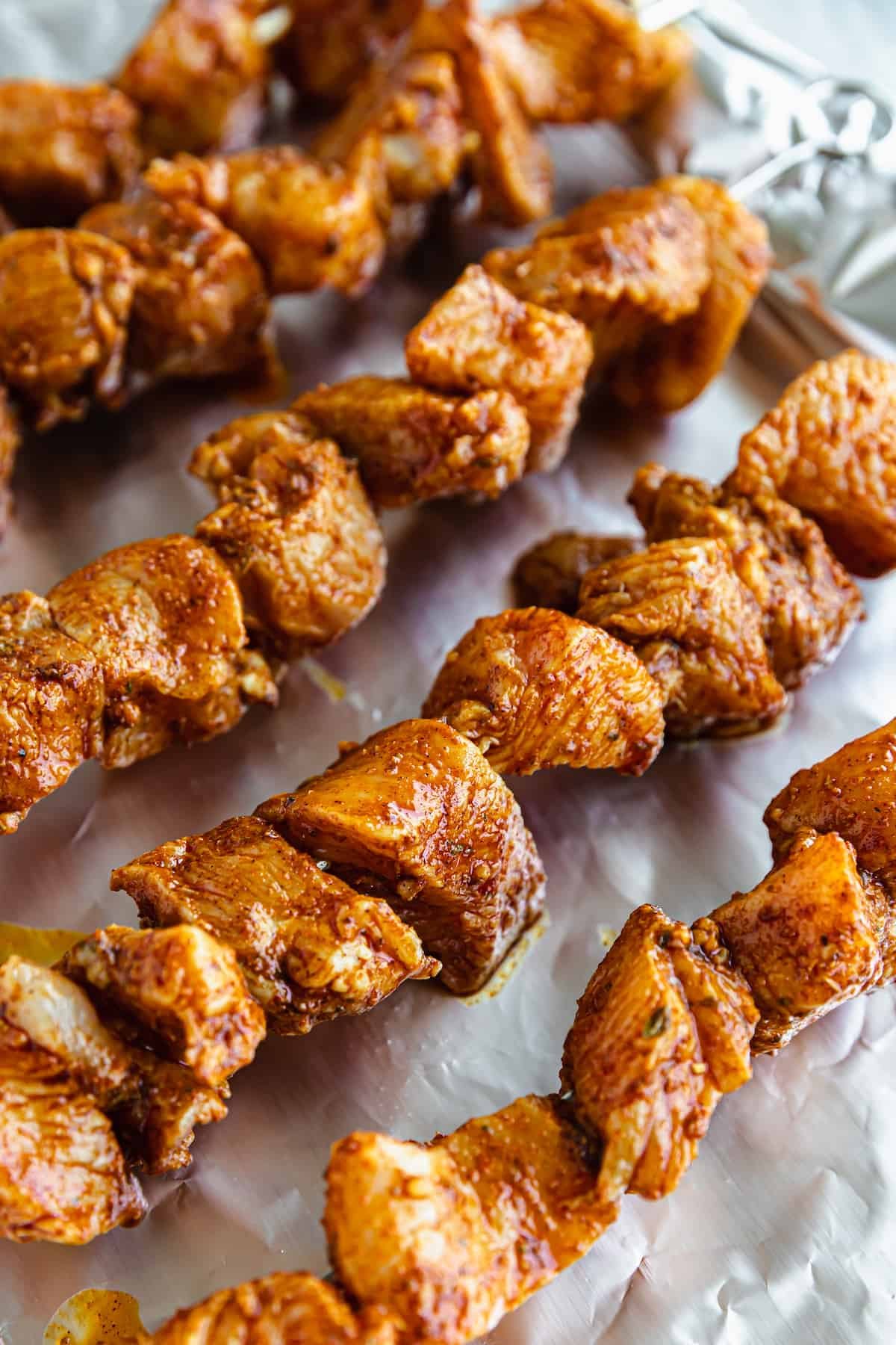 Five Freshly Grilled Shawarma Chicken Skewers Lined Up on a Sheet of Aluminum Foil