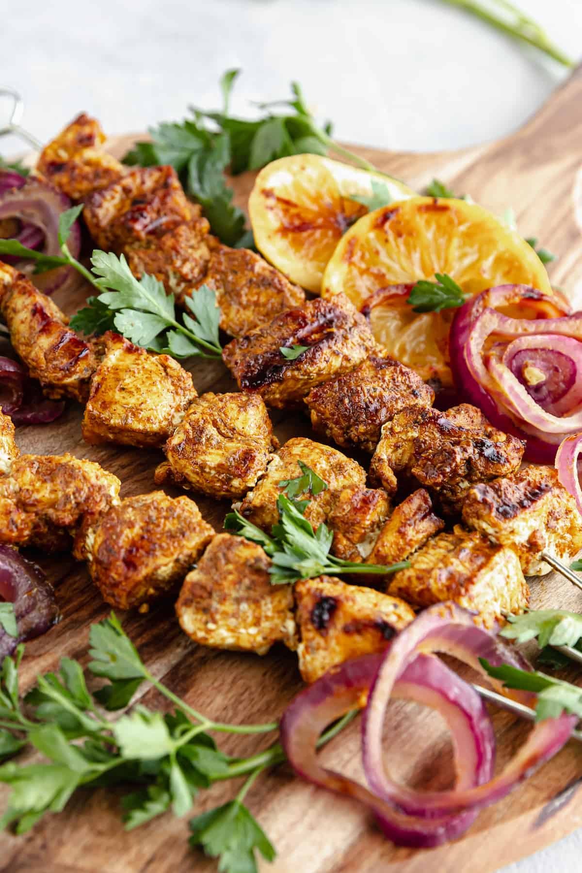 A Cutting Board on a Table Holding Onions, Lemon Slices and Shawarma Grilled Chicken Skewers