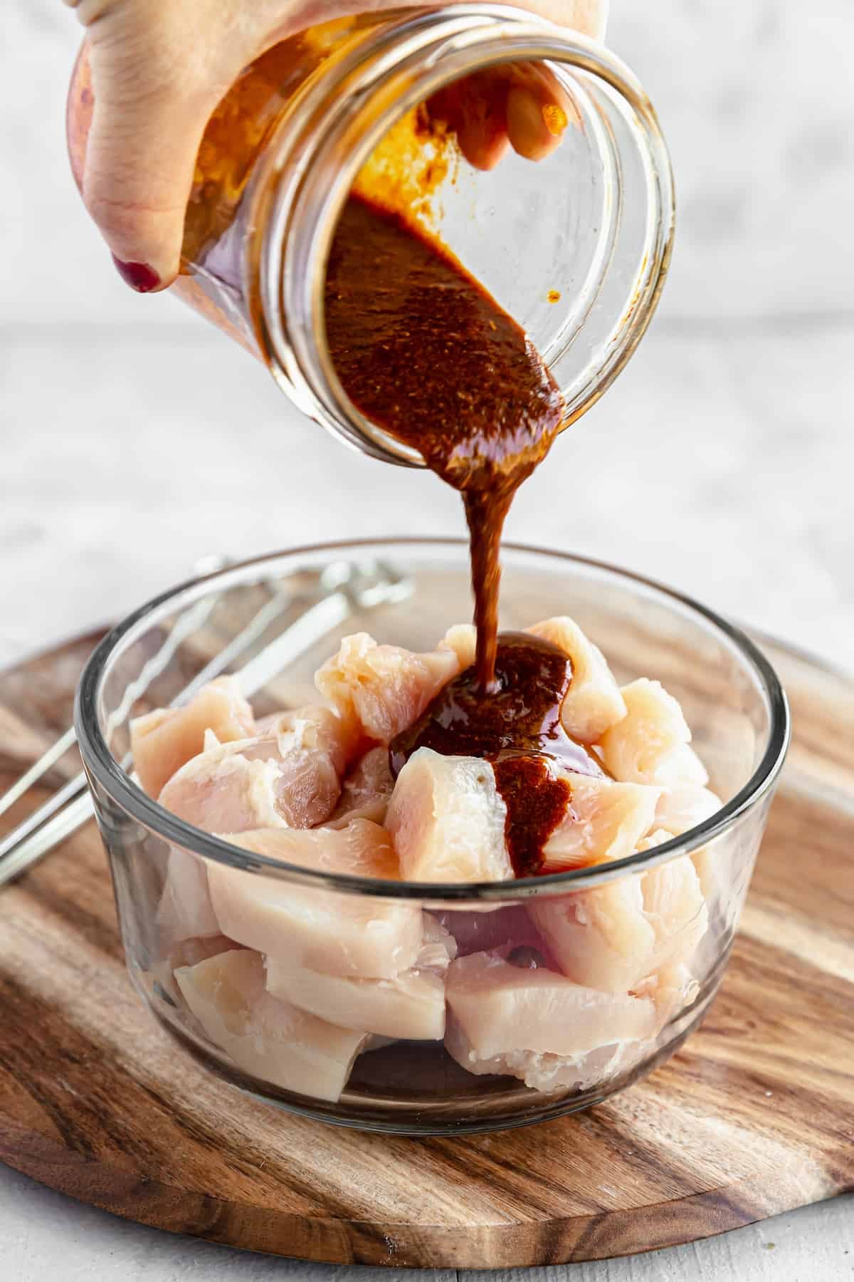A Dish of Raw, Cubed Chicken Breast with a Jar of Shawarma Marinade Being Poured Into it