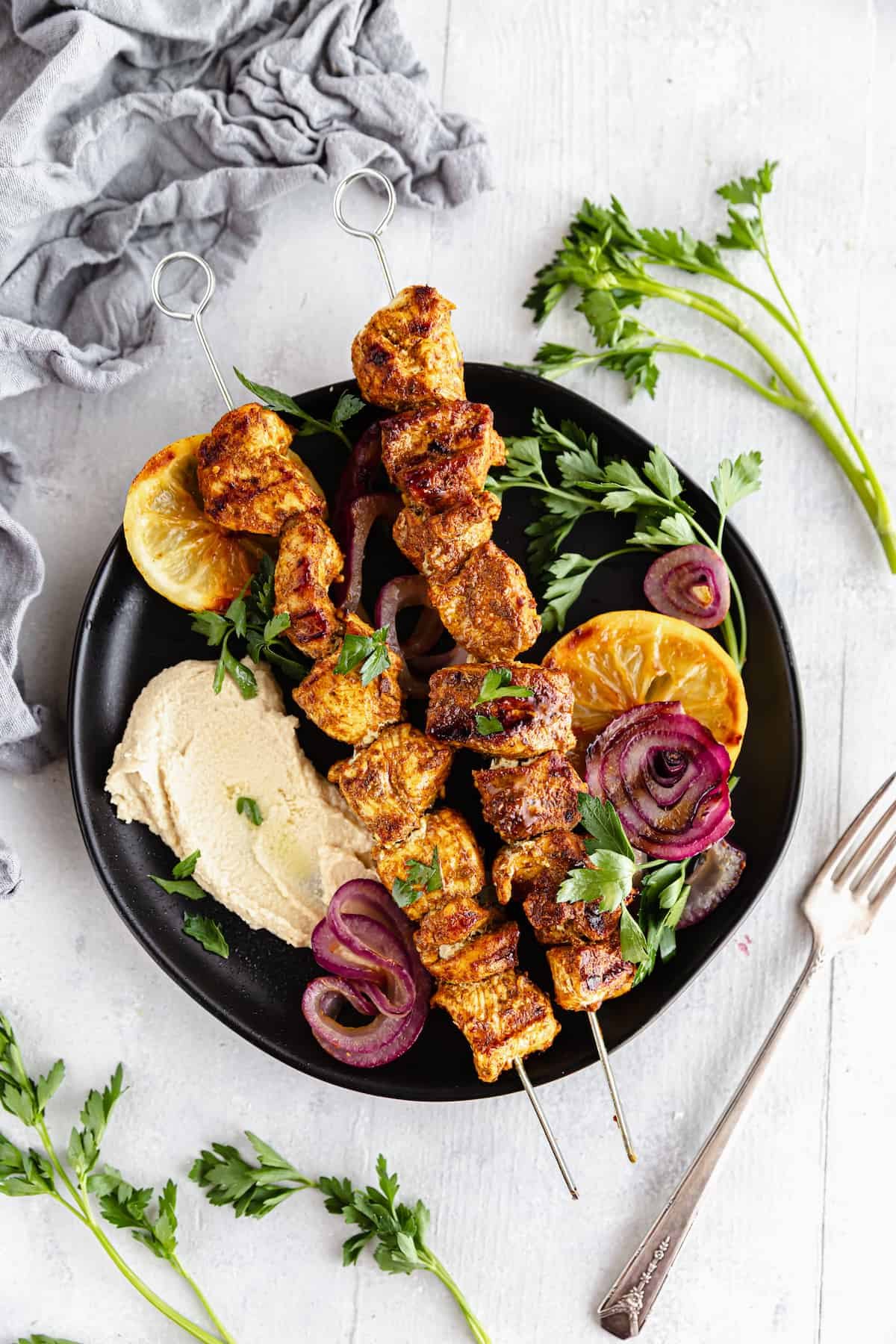A Black Plate Containing Two Chicken Skewers Along with Various Fruits and Vegetables with a Fork Beside it