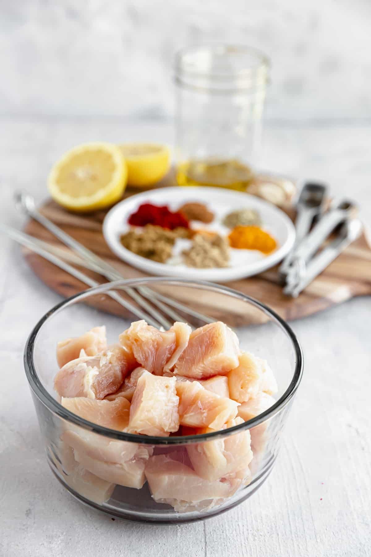 Cubes of Boneless, Skinless Chicken Breast with Spices and the Remaining Kebab Ingredients in the Background