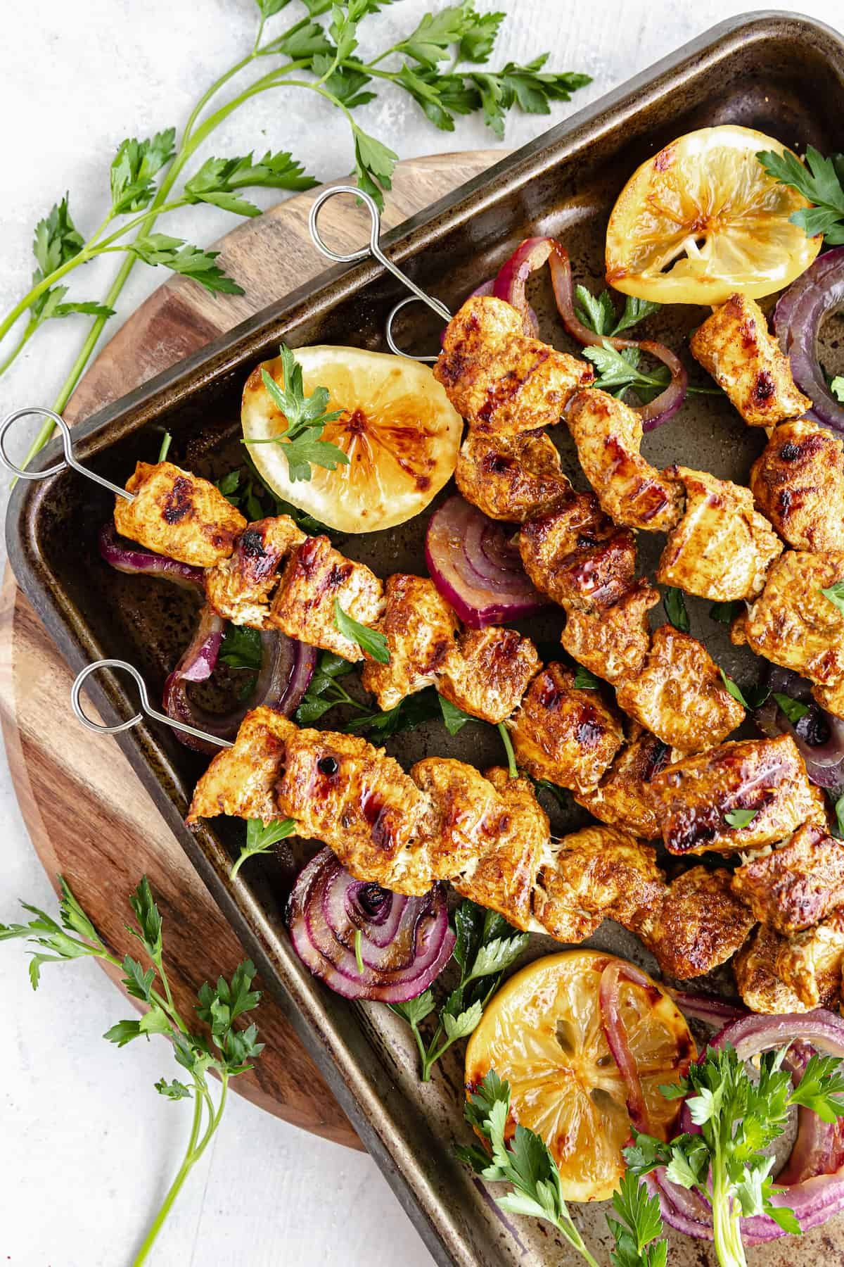 Grilled Chicken Skewers in a Pan on Top of a Round, Wooden Cutting Board