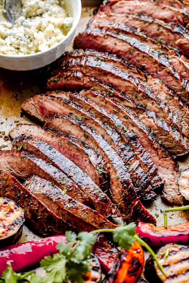 side close up shot of sliced grilled flank steak with a white bowl next to it