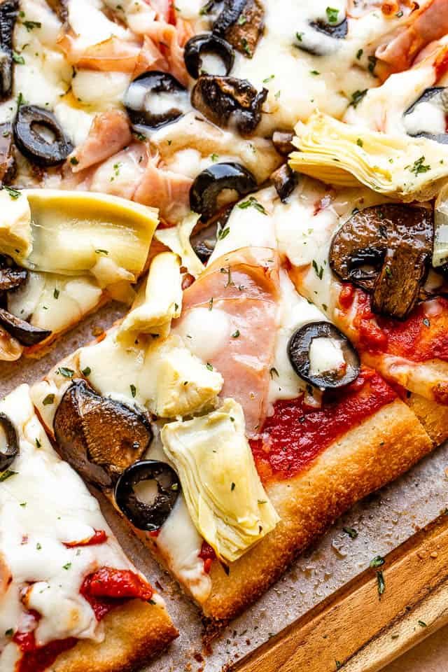 top view of square slice pizza topped with ham, olive slices, and artichoke hearts
