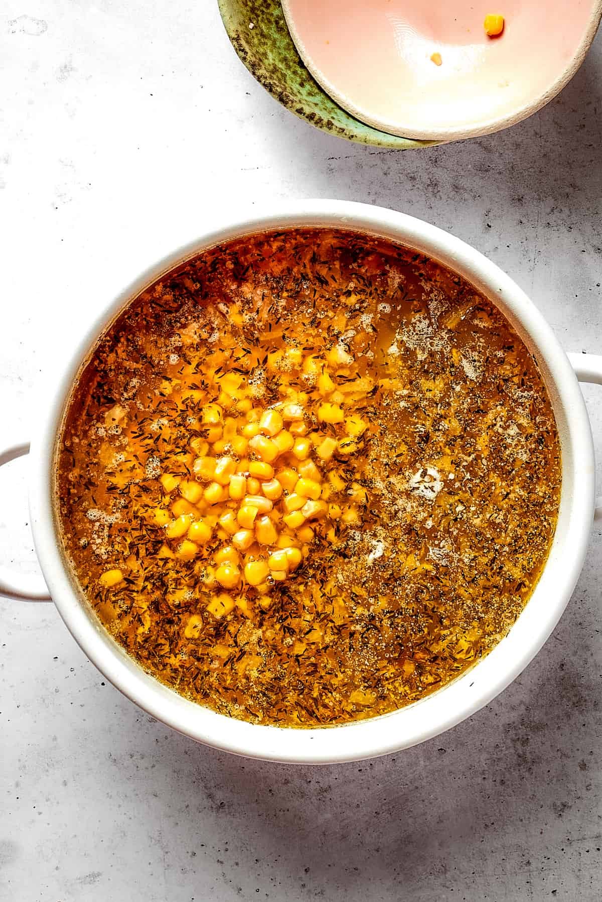 Overhead view of a Dutch oven filled with soup, with corn and white kidney beans on top, next to two empty bowls.