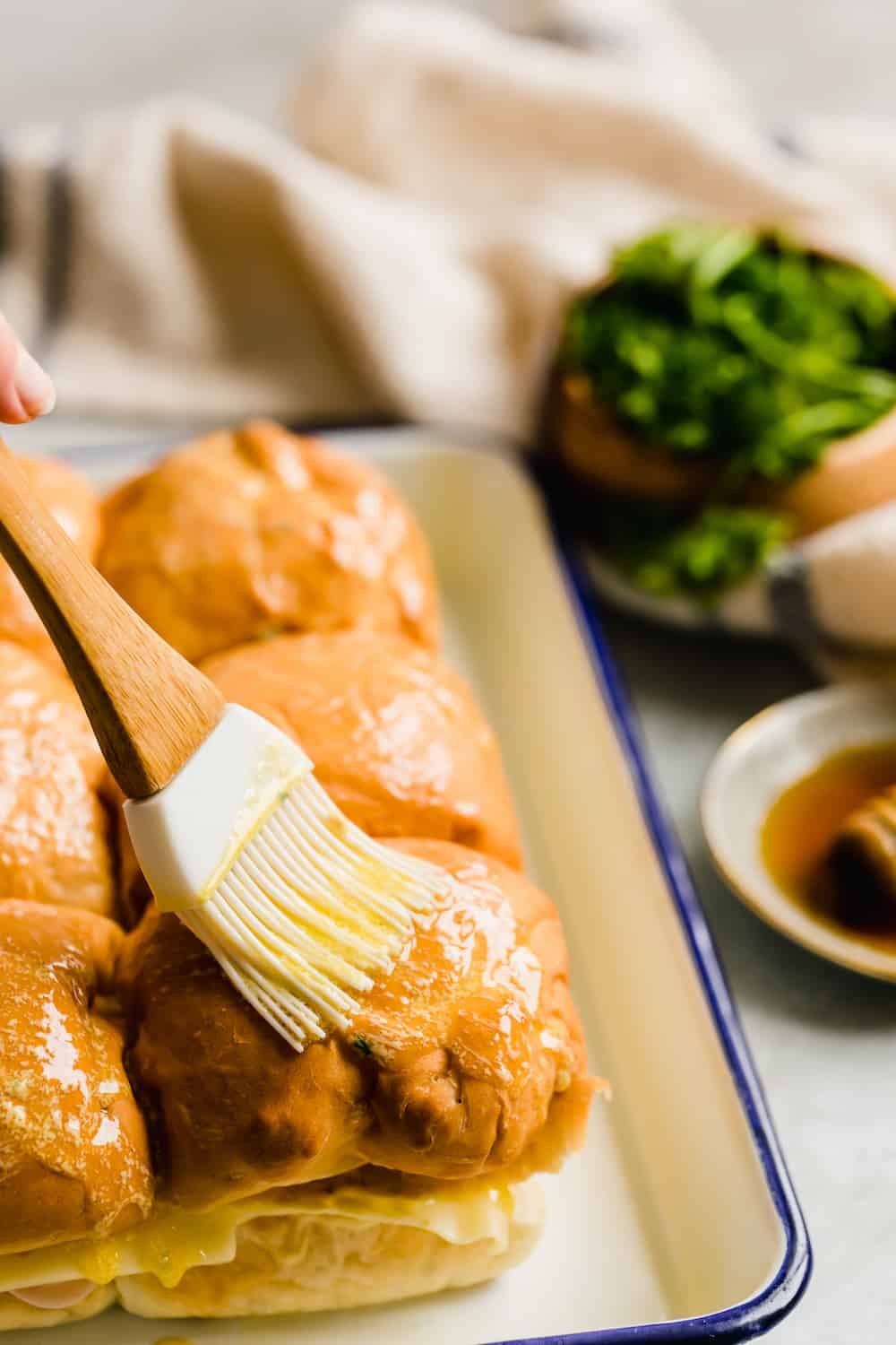 Melted Butter and Mayo Being Brushed Over Six Hawaiian Rolls