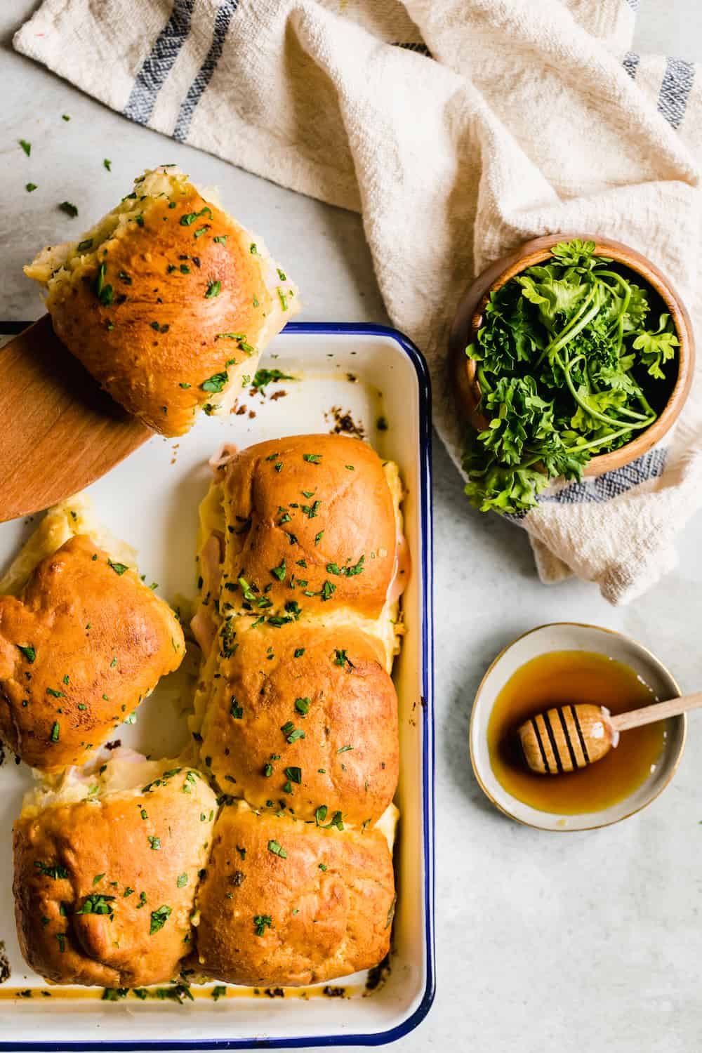 A Pan Full of Ham Sandwiches Beside a Small Bowl of Fresh Honey