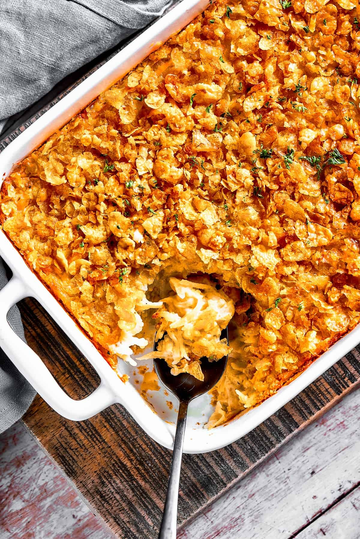 A casserole dish with hashbrown casserole. Some of it has been spooned out, and a serving spoon is set inside the casserole dish.