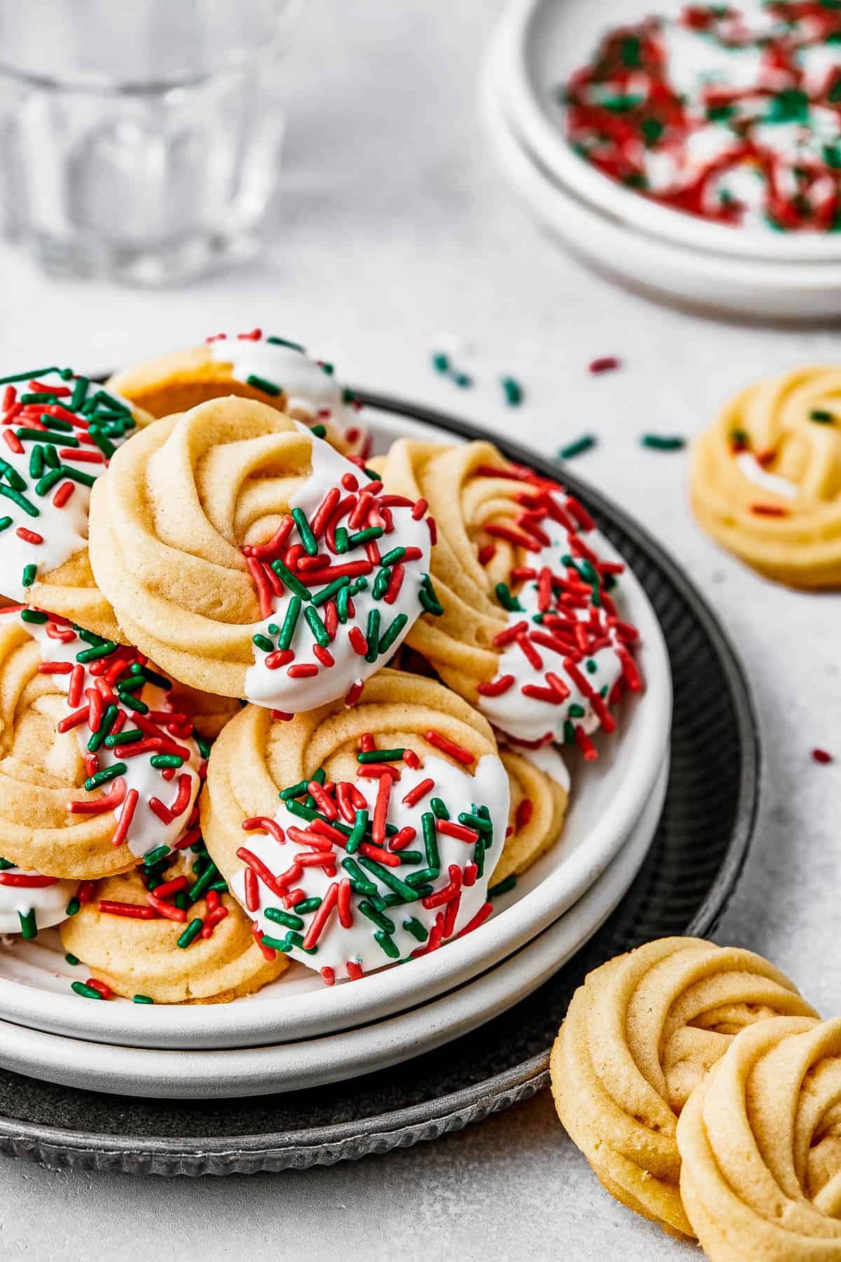A small dessert plate stacked on top of several other plates, and piled with iced butter cookies.
