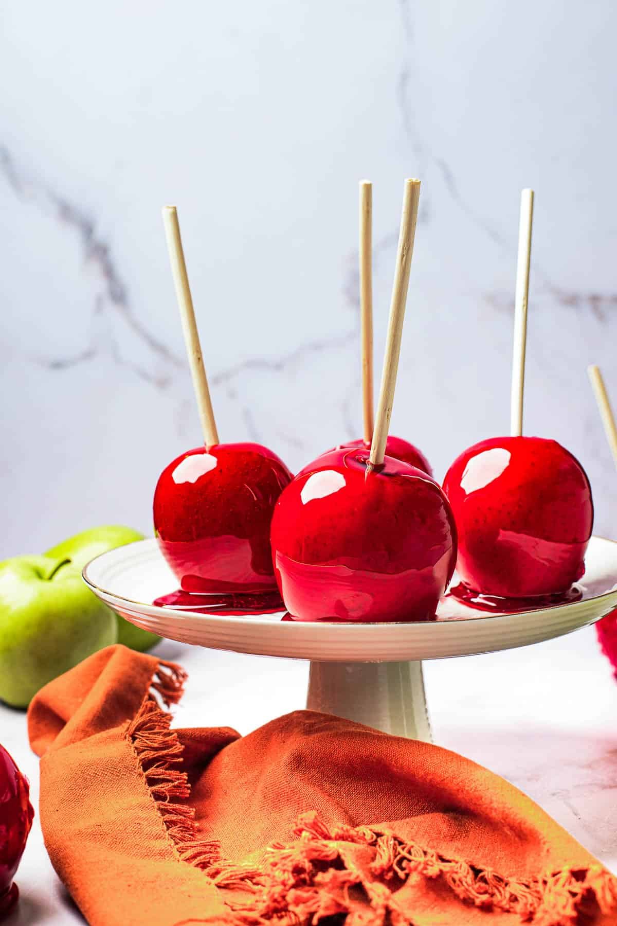 A white cake stand with four candied apples displayed on it.