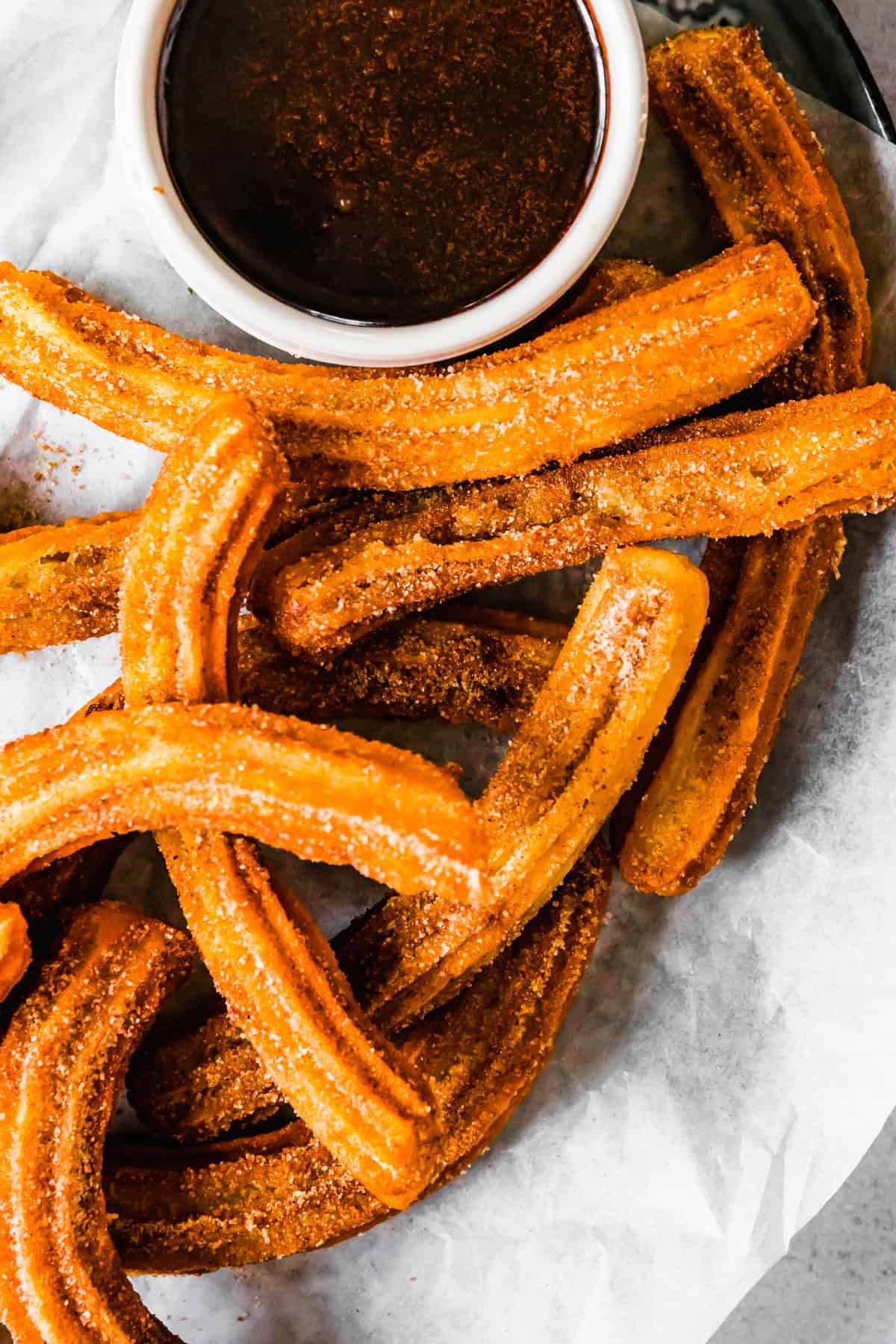 Churros recipe by easy weeknight recipes. The churros are served on a plate with a bowl of chocolate sauce.