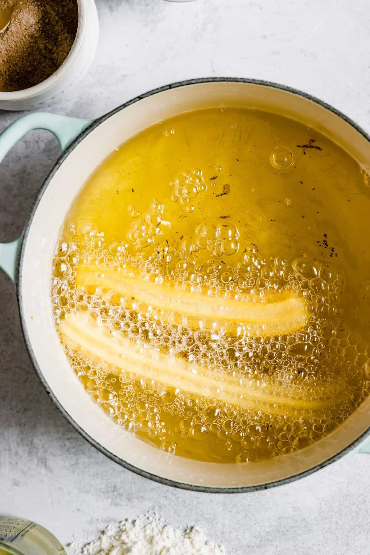 Two Churros Frying in a Pan Filled with Oil