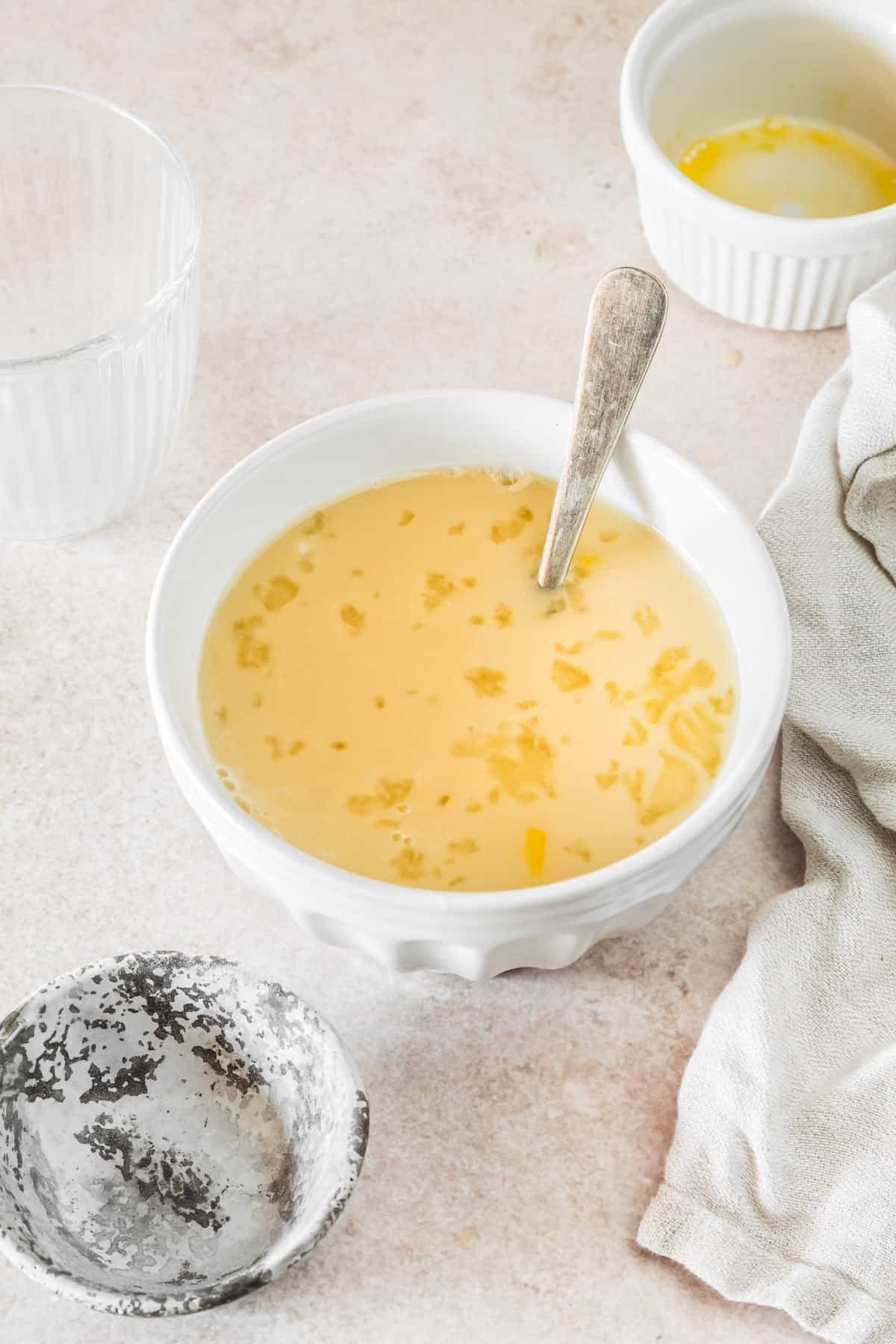 A small mixing bowl with egg, milk, yeast, and water mixed together. A floury spoon and dish towel are on the work surface.
