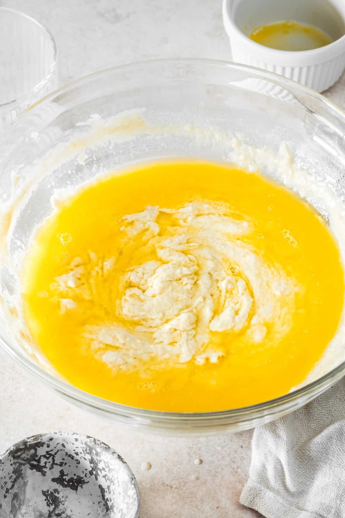 A mixing bowl with dough and melted butter inside.