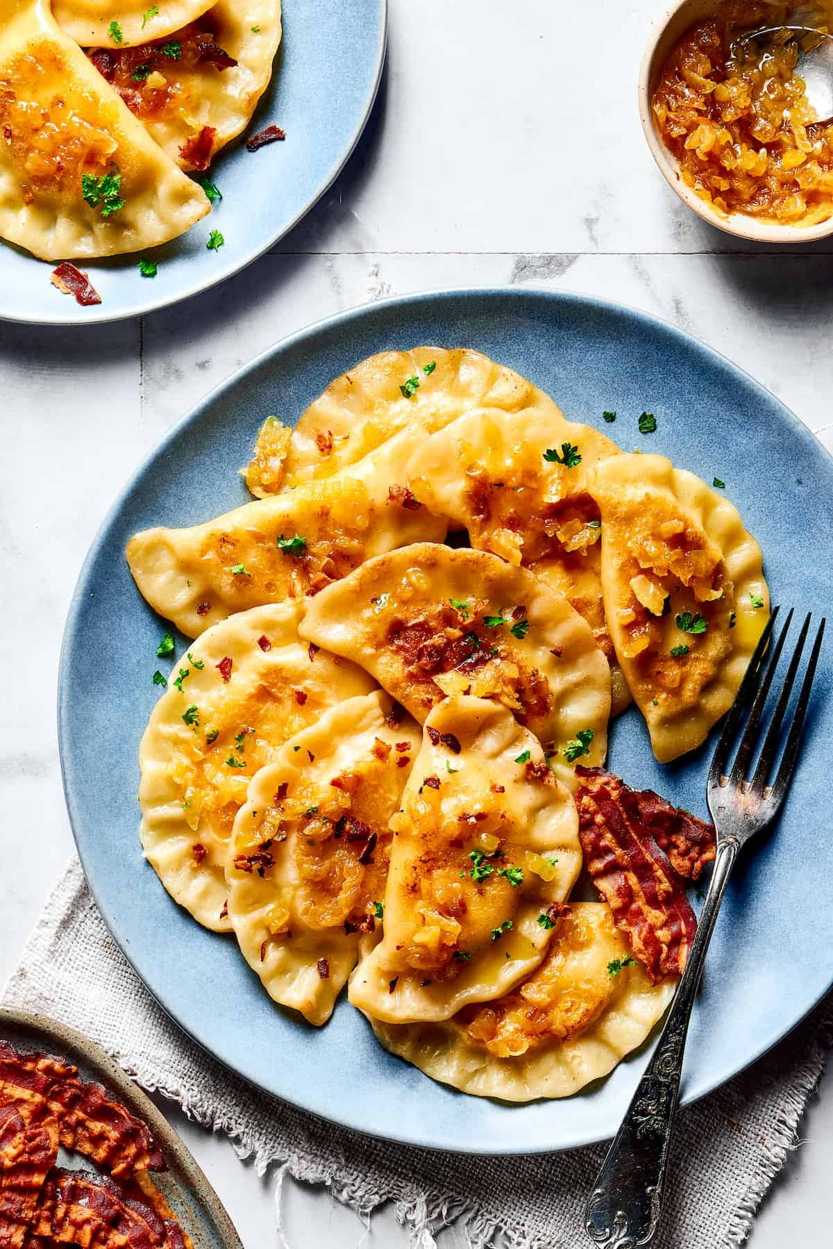 Cooked pierogi topped with bacon and onions.
