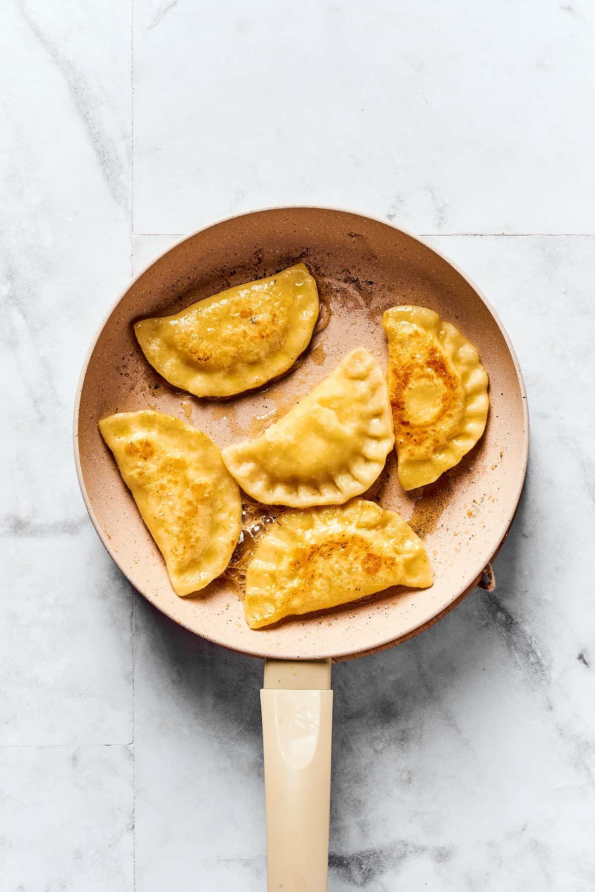 A skillet of pierogi frying in butter.