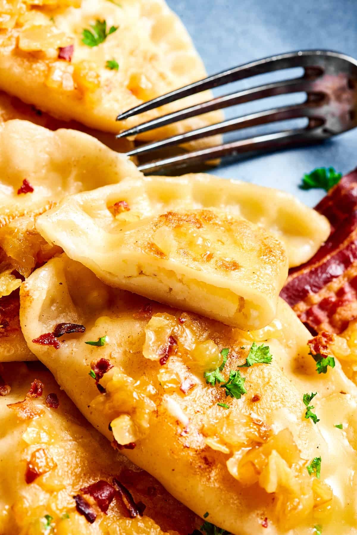A plate of pierogies. One has been cut in half with a fork.