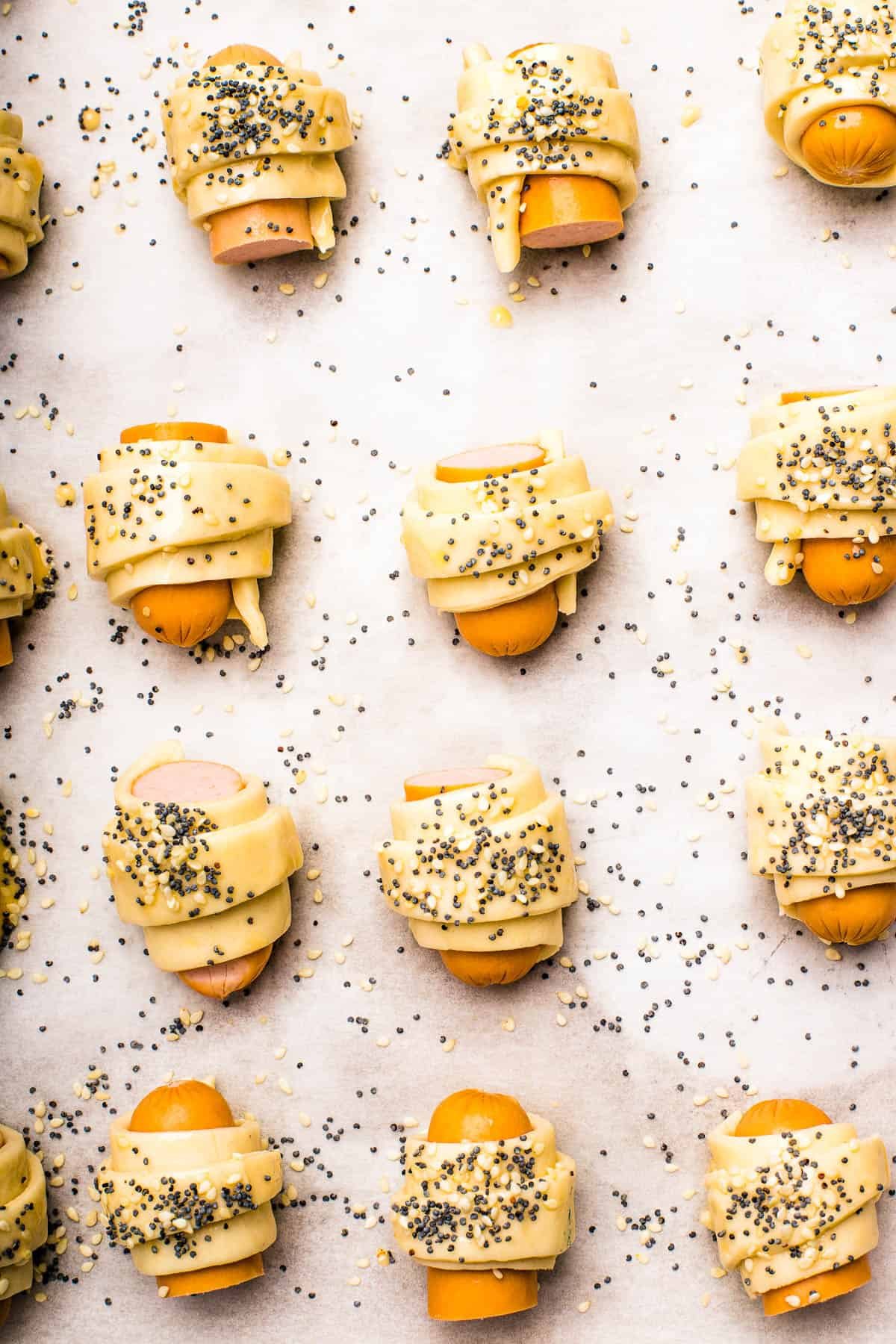 Unbaked pastries brushed with egg wash and sprinkled with sesame seeds and poppy seeds.