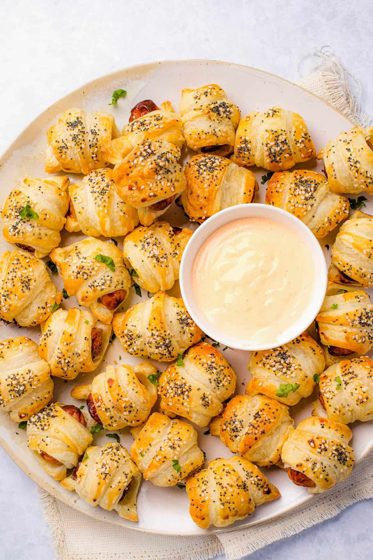 A platter of pigs in a blanket with a bowl of dipping sauce in the center.