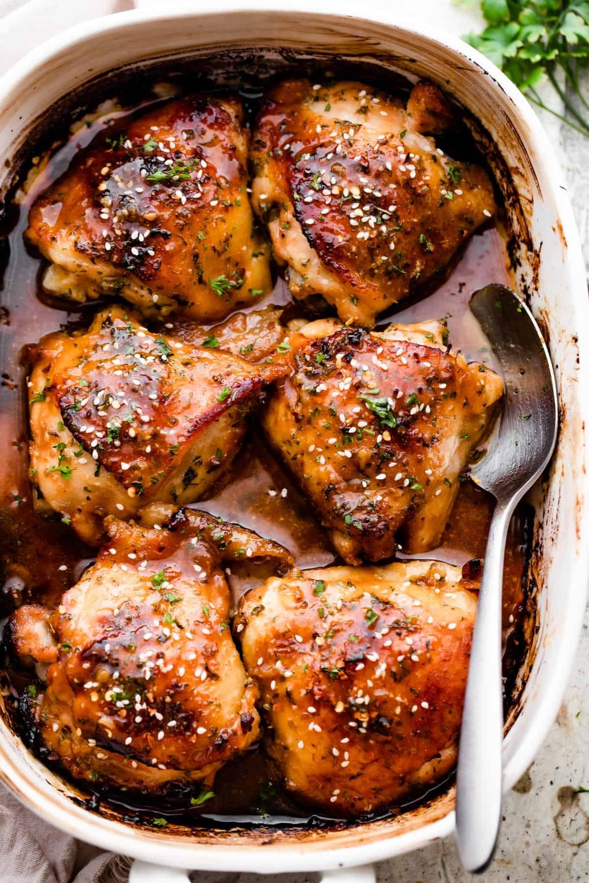 overhead shot of a baking dish with six honey garlic baked chicken thighs garnished with sesame seeds.