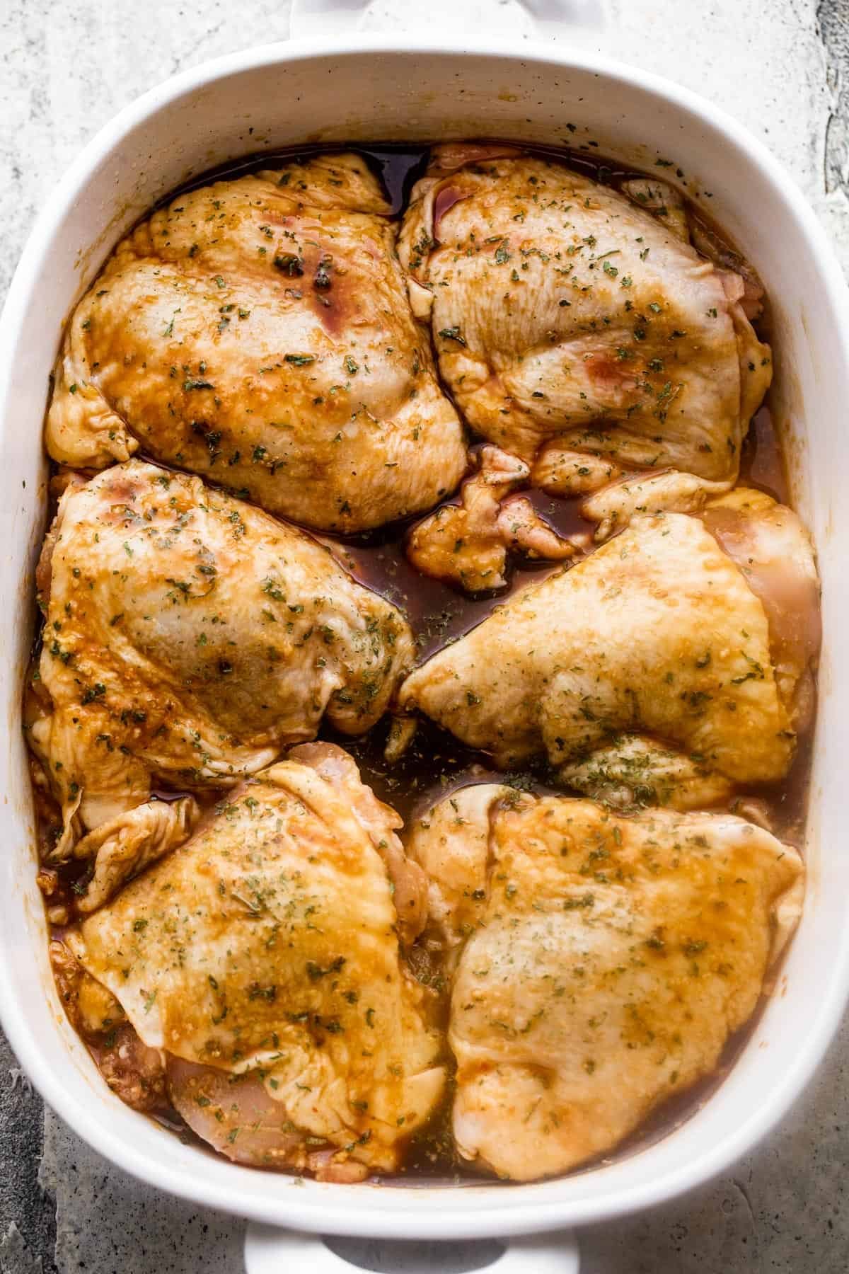 Overhead image of a white baking dish with six raw bone-in, skin-on chicken thighs arranged inside of the baking dish.