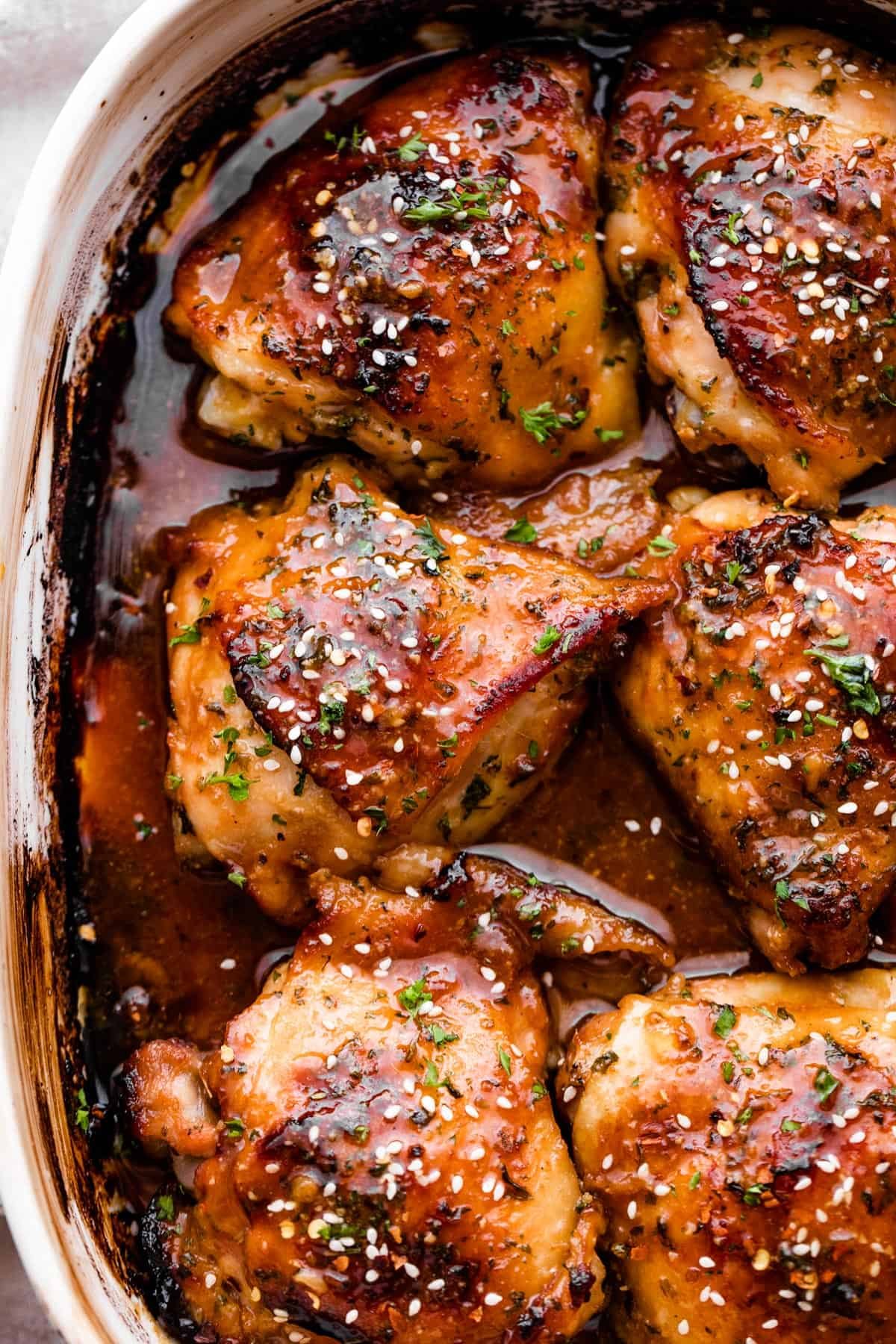 overhead shot of a baking dish with six honey garlic baked chicken thighs garnished with sesame seeds.