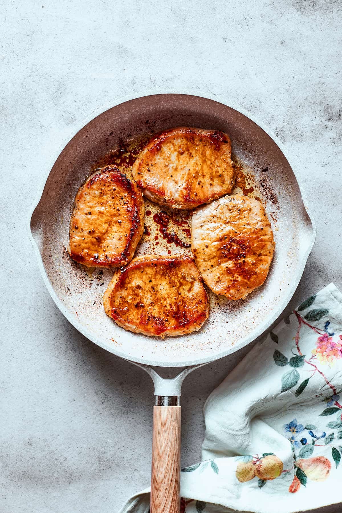 Pork chops sear in a white skillet.
