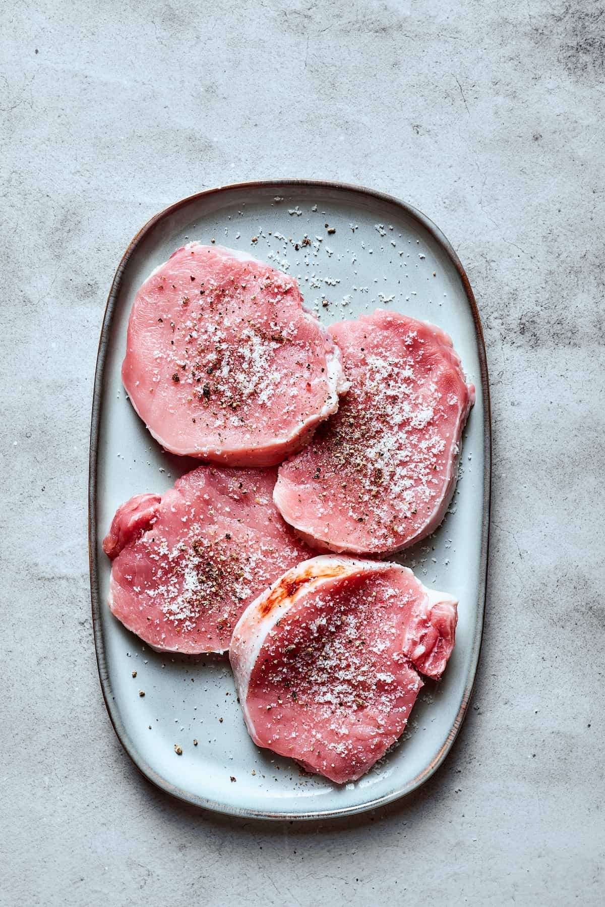 Pork chops seasoned with salt and pepper on a white tray.