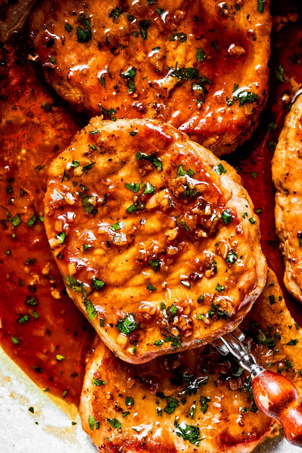 Close-up image of a spoon holding up a pork chop.