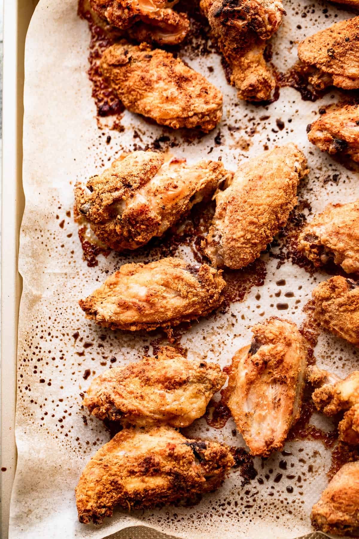 overhead shot of cooked hot wings arranged on a parchment lined baking sheet.
