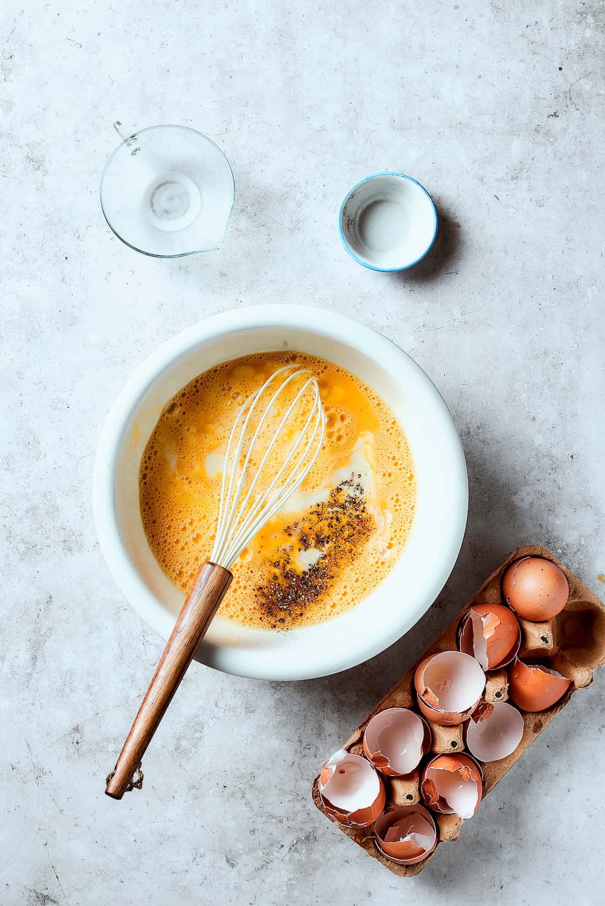Adding salt, pepper, and milk to eggs in a mixing bowl.
