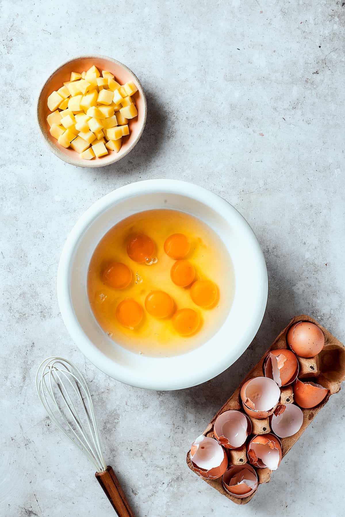 Eggs cracked into a bowl, with cooked potatoes nearby on the table.