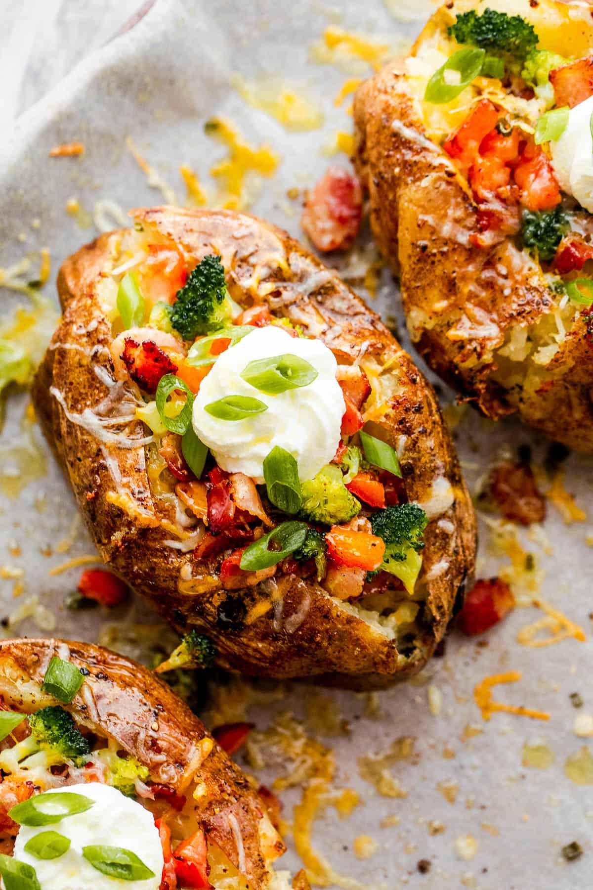 Three Instant Pot Baked Potatoes Beside Bowls of Cheese, Broccoli, Bacon, Chopped Green Onions and Sour Cream